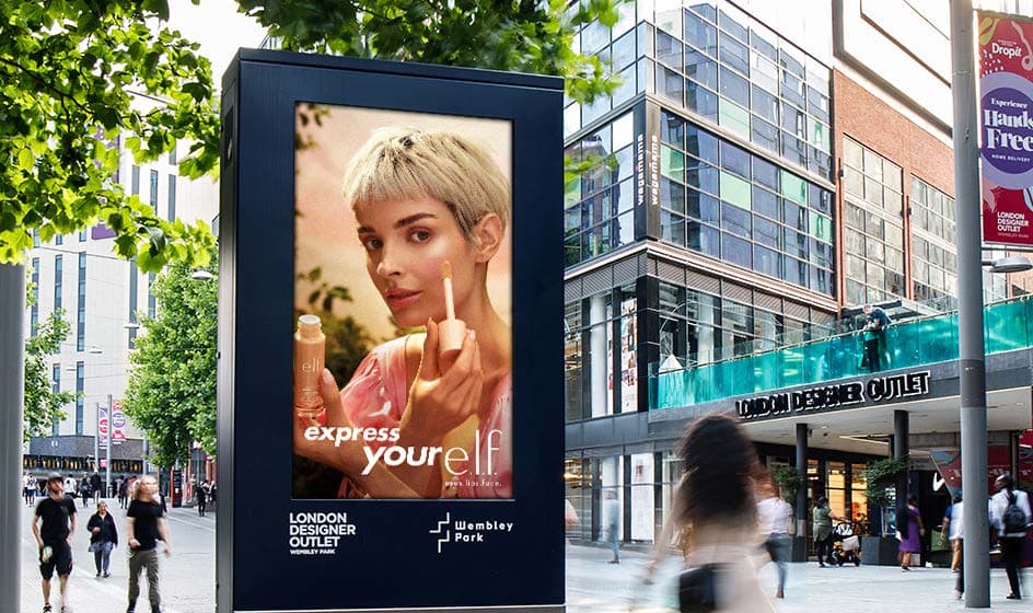 Digital screen beside shoppers at London Designer Outlet, Wembley Park